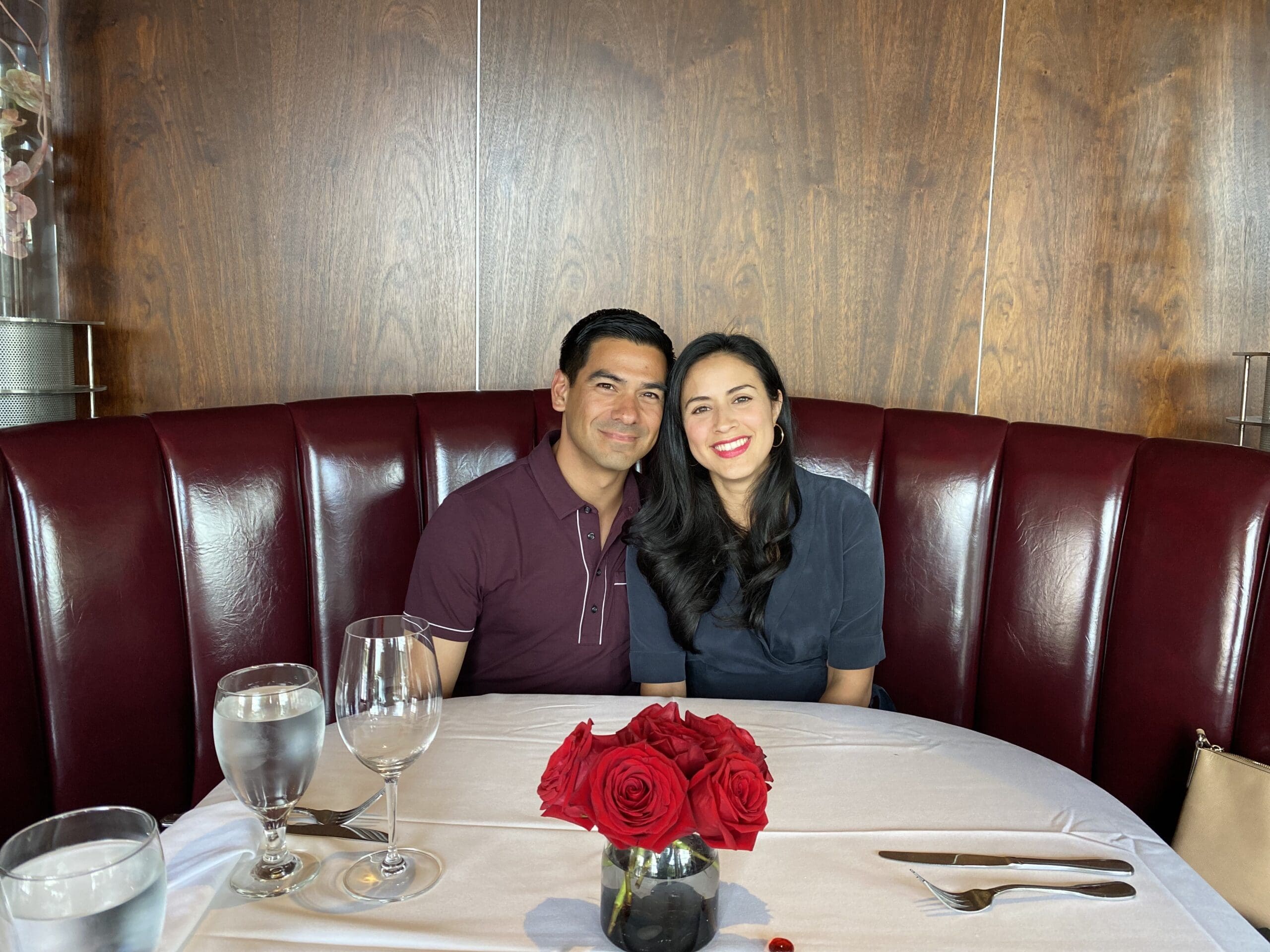 husband and wife sitting at a restaurant in a booth with red roses in a vase